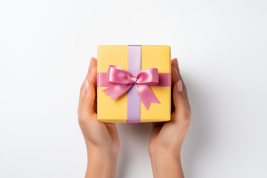 Top view of hands holding craft paper gift box with ribbon bow on isolated pastel blue background. Generated AI.