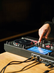 Obraz premium Hand of a DJ mixing music tracks on DJ controller with a black background.
