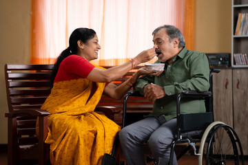 happy caring wife feeding her husband with disability on wheelchair at home - concept of health...