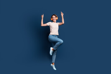 Fototapeta na wymiar Full length photo of lovely young lady jump dancing headphones have fun wear trendy white garment isolated on dark blue color background