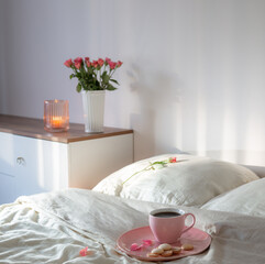 pink cup of coffee on bed with flowers in vase  in white bedroom