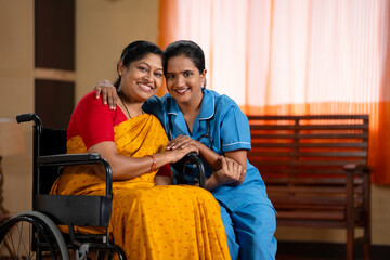 Happy recovered woman on wheelchair with caretaker looking camera at home - concept of professional...