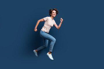 Fototapeta na wymiar Full length photo of lovely young lady running hurry have fun shopping wear trendy white garment isolated on dark blue color background