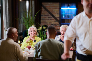 A group of family friends, comprising a young grandson and older individuals, share a delightful dinner in a modern restaurant, exemplifying the concept of healthy aging through intergenerational