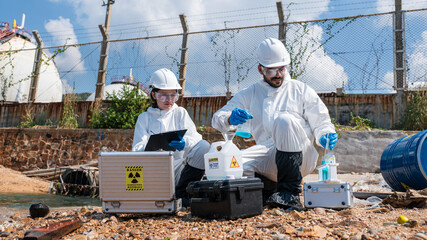 Scientists biologists and researchers in protective suits taking water samples from waste water...