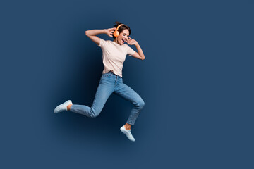 Fototapeta na wymiar Full body photo of pretty young girl running jump excited dance headphones wear trendy white outfit isolated on dark blue color background