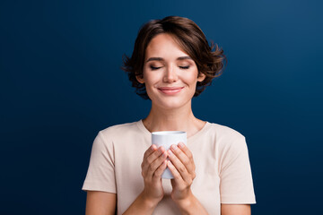 Photo portrait of attractive young woman hold coffee mug smell aroma dressed stylish white clothes isolated on dark blue color background