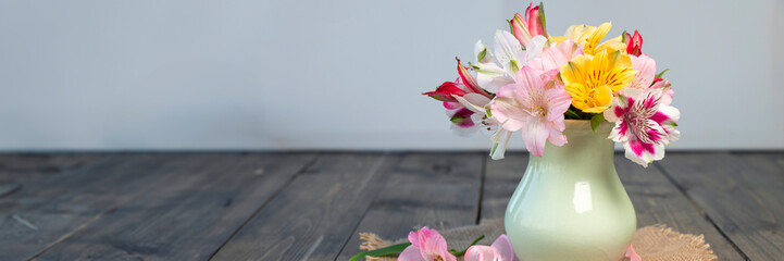 banner of multi-colored blooming alstroemeria flowers in clay vase on wooden table with round...