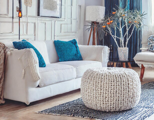 Two knitted poufs near white corner sofa. Scandinavian home interior design of modern living room