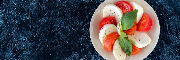 banner of caprese salad on a round plate. slices of juicy red tomato, with fresh mozzarella and...
