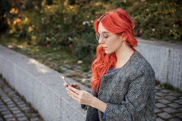 Young red haired business confident  woman using smart phone outdoor of the city sunset background. 