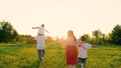 Fototapeta na wymiar Family, mom dad and children play together, happy childhood. Active family, raising their hands, runs towards sun, dreams of flying in natural park, sunset. Slow motion. Happy people, childrens future