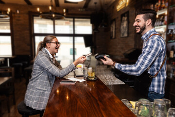 Business woman paying with a contactless debit credit card in a restaurant, waiter or barman holding a payment terminal. Transaction without contact, female pay for coffee or tea in coffee shop. - Powered by Adobe