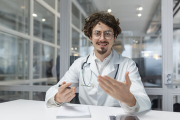 A doctor wearing a white lab coat and a stethoscope is sitting at a table inside a medical office....