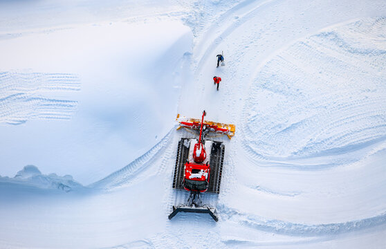 Snow groomer in white surrounding. Special vehicle preparing snow for ski jumping in “Mühlenkopfschanze“ arena in Willingen, Germany. Arial view of from popular touristic suspension bridge above.