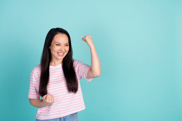 Fototapeta premium Photo of sweet lucky mixed race mestizo lady dressed striped t-shirt rising fists looking empty space isolated teal color background