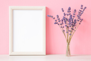 Dry purple lavender in glass vase on light table at pink wall background. Pastel color. Closeup. Empty place for inspirational, sentimental text, quote or sayings in white frame. Front view.