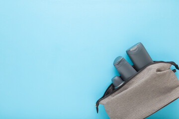 Dark gray plastic bottles in cosmetic travel bag on light blue table background. Pastel color. Care...