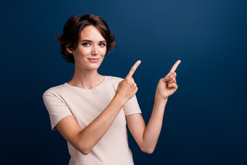 Obraz premium Portrait of attractive girl promoter directing fingers arms empty blank space promotion isolated on dark blue color background