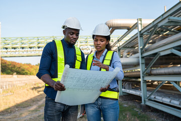 Young mechanical engineer holding blueprint drawing to checking and inspection gas pipeline system new construction project of industrial.