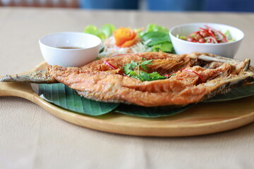 Deepfried sea bass with fish sauce served with mellow dipping sauce with sliced ​​mango to add flavor and fresh vegetables arranged in wooden plate. Deep-fried sea bass with fish sauce is popular dish