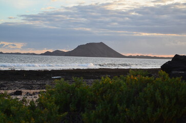 Beautiful sunrise over the Atlantic Ocean near the town of Corralejo, on Fuerteventura beach overlooking the islands of Lobos and Lanzarot. Rocky beach in the morning with a view of the rolling sea