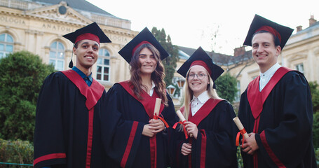 Portrait shot of the young happy male and female students graduates in academic caps and gowns and...