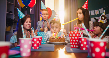 Happy little boy celebrating birthday with friends at home, blowing candles at cake , making wish...