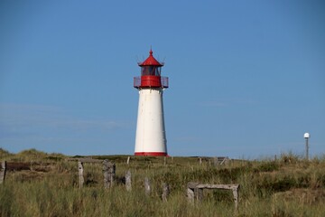 Ellenbogen lighthouse on sand dune against blue sky with white clouds on northern coast of Sylt...