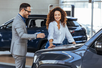 Woman in the showroom enjoying luxury car. Happy salesman selling the car to his female customer in...
