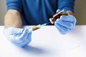 Doctor's or nurse's hands, on white table and wearing blue gloves, are holding syringe as he...
