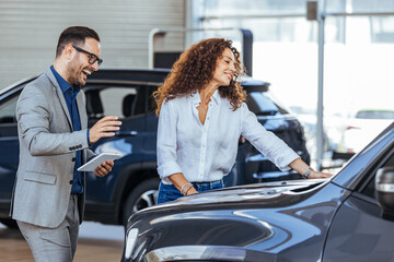Woman in the showroom enjoying luxury car. Happy salesman selling the car to his female customer in a showroom. Male sales manager selling electric car to a female customer at showroom