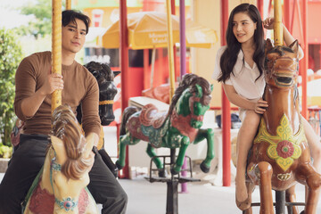 couple asian man and woman dating and riding on horse at Carousel amusement park. Concept happy and lovely life of teenager.