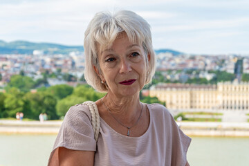 A thoughtful and sad elderly woman of 60-70 years old with gray hair against the background of a picturesque landscape of the city.