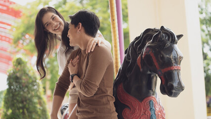 Young joyful couple man and woman riding on horse at Carousel amusement park. Concept happy and...
