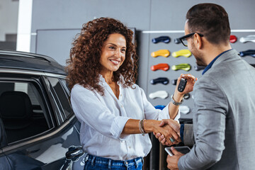 Salesman giving new car keys to female customer. Car dealer is giving key for a new car to a woman. 