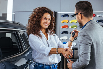 Smiling woman receiving her car keys in auto saloon. Happy salesman congratulating his female...