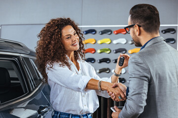 Salesman giving new car keys to female customer. Car dealer is giving key for a new car to a woman....