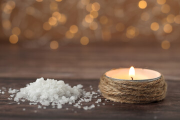Sea salt and candle burning with bright flame with bokeh light background. Close-up. Selective...
