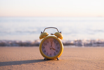 Yellow alarm clock on the beach in the sunset time. The concept about Time to summer, Travel,...