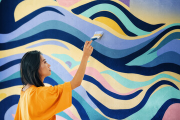 Female street artist painting bright colorful graffiti on wall