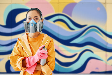 Graffiti female street artist in respirator mask standing near the wall with her paintings looking...