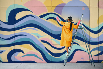 Female street artist painting colorful graffiti standing on a ladder
