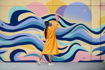 Female street artist painter in respirator mask painting colorful graffiti on wall