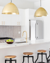 A kitchen detail with white cabinets, gold faucet and light hanging over the island with bar...