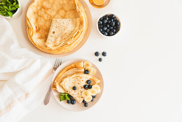 French crepes with banana and blueberries on white table. Top view