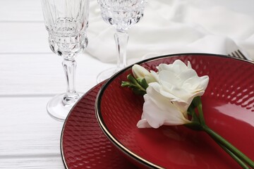 Dishes with flower and glasses on white wooden table, closeup