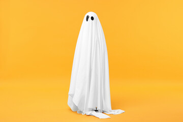 Child in white ghost costume on orange background. Halloween celebration