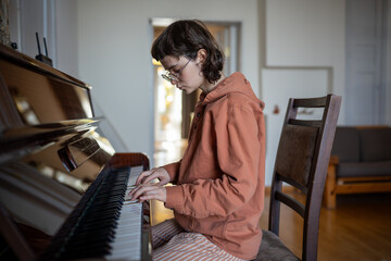Teenager sitting on chair, playing piano, improvising, practicing skills at home lesson, learning...