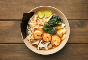 Delicious ramen with shrimps and mushrooms in bowl on wooden table, top view. Noodle soup
